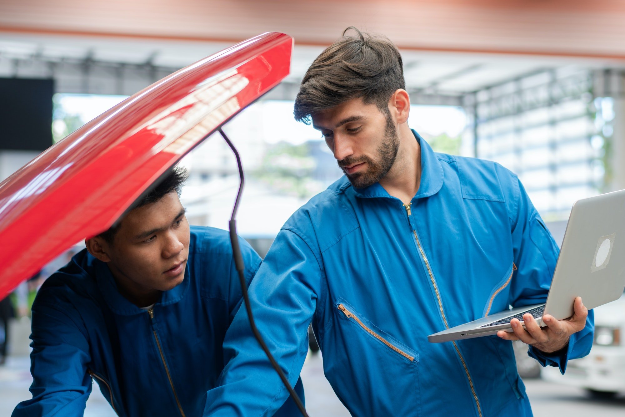 Car Mechanic Team Using Laptop Boosting Car Engine At Auto Repair Shop