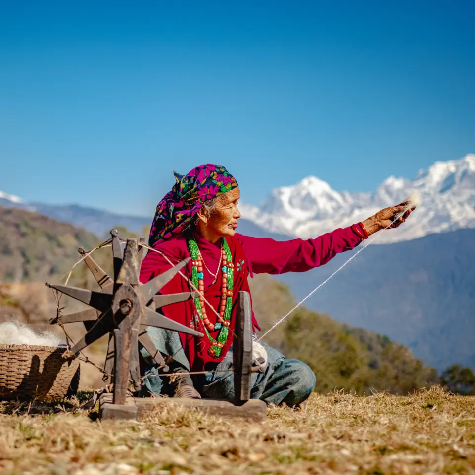 Idosa Nepalesa Tecendo Algodão Em Um Dia Ensolarado, Com A Cordilheiraannapurna, No Nepal, Ao Fundo. - Imagem: Shutterstock/Keshav Dulal